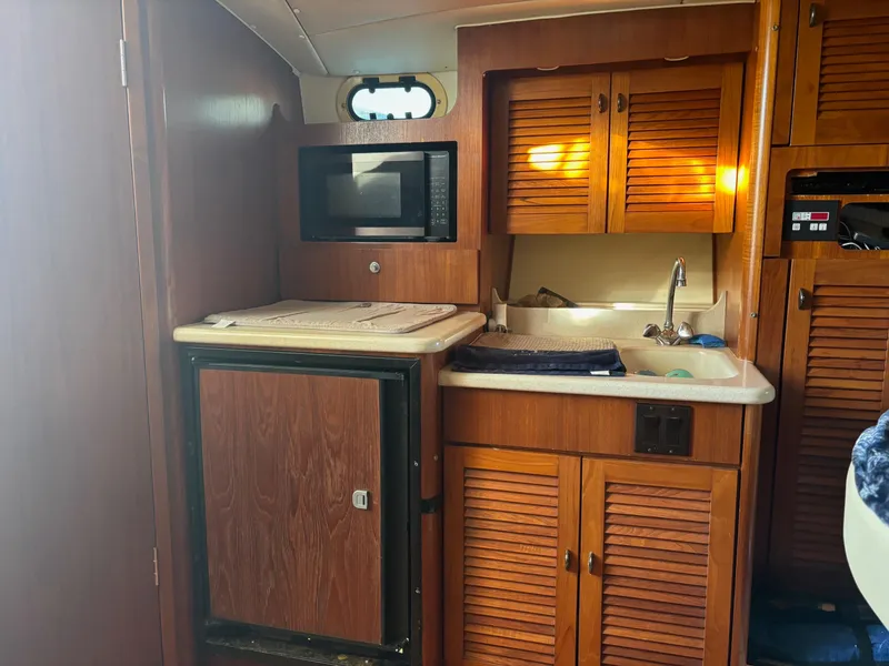Slide: The Image of 2000 Pursuit 3400 Express boat kitchen with wood cabinets, microwave, and sink. - 22