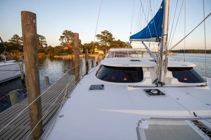 Slide: The Image of 2004 Antares PDQ 44 catamaran docked by a serene waterfront with trees. - 2