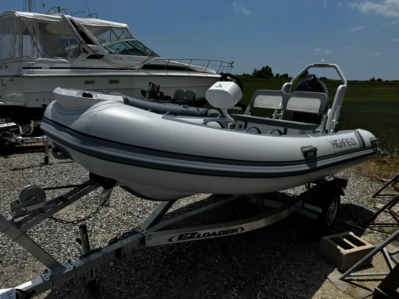 Slide: The Image of 2025 Highfield Classic 400 inflatable boat on trailer, parked beside larger yacht. - 4