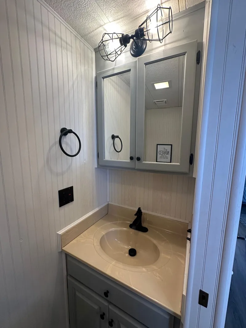Slide: The Image of Small bathroom vanity with mirror, industrial light fixture, and beige countertop in Lakeview 15x70, 1995. - 12