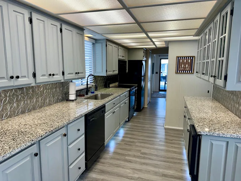 Slide: The Image of Modern kitchen with granite countertops, light cabinetry, and stainless steel appliances in a Lakeview 15x70 model. - 4