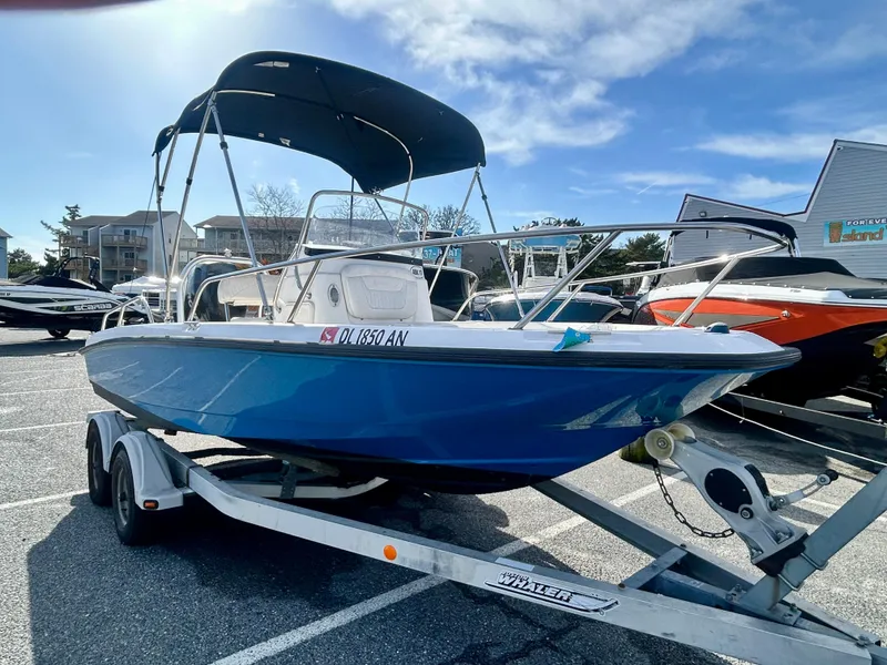 Slide: The Image of 2011 Boston Whaler DAUNTLESS 180/CC boat on trailer, blue hull, bimini top, parked outdoors. - 3