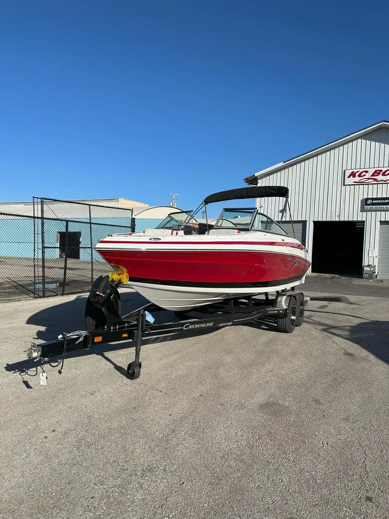 The Image of 2025 Crownline 240 SS boat on trailer, red and white, parked outside a building. - 0