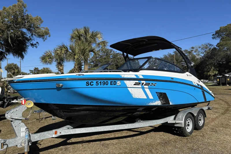 Slide: The Image of 2021 Yamaha Boats 212XE on trailer, blue and white design, parked outdoors. - 1