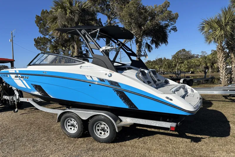 Slide: The Image of 2021 Yamaha Boats 212XE on trailer, vibrant blue and white design, parked outdoors. - 2