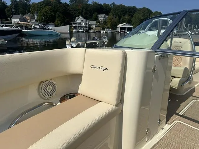 Slide: The Image of 2021 Chris-Craft Launch 27 boat interior with beige seating, docked by a scenic waterfront. - 16