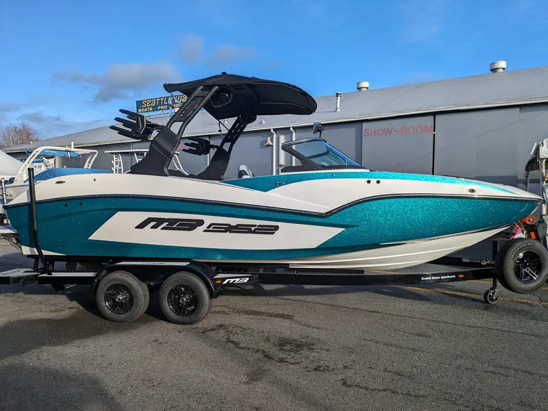 The Image of 2025 MB B52-23 Alpha boat on trailer, teal and white design, parked outdoors. - 0