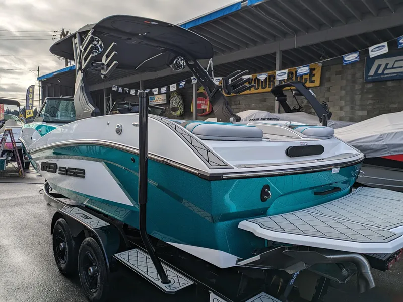 Slide: The Image of 2025 MB B52-23 Alpha boat on trailer, teal and white design, under a covered area. - 5