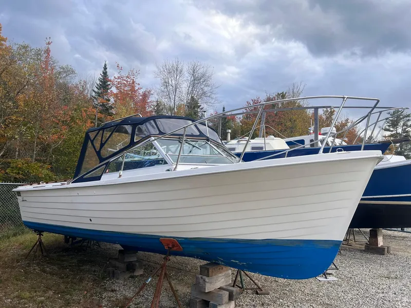 Slide: The Image of 1975 Lyman 26 Cruisette boat on stands, surrounded by autumn trees and cloudy sky. - 2