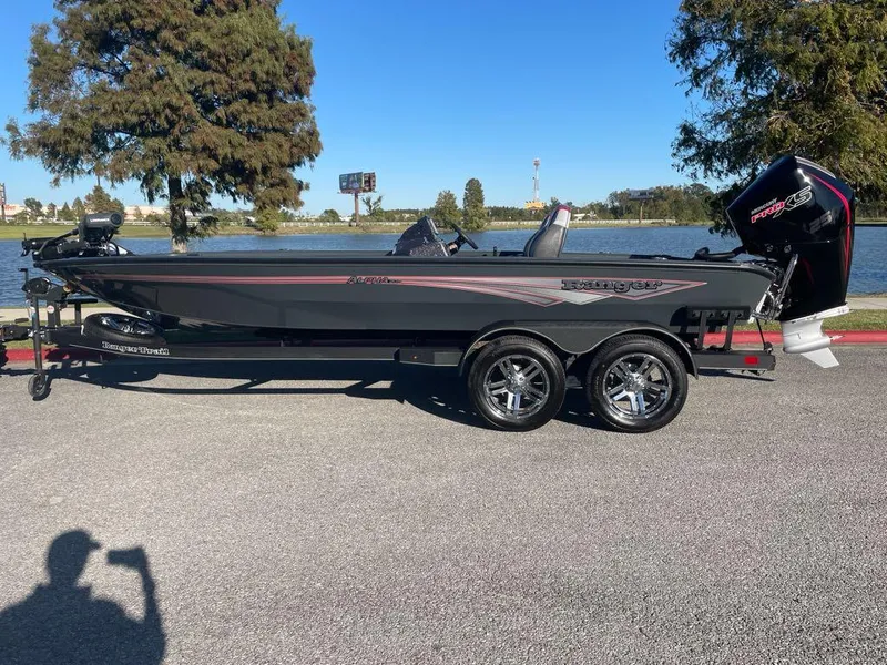 The Image of 2025 Ranger ALPHA 208 boat on trailer, parked near a lake with trees in the background. - 0