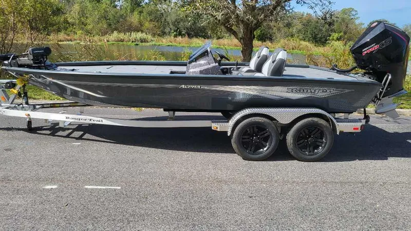 Slide: The Image of 2025 Ranger ALPHA 208 boat on trailer, parked on road near trees and water. - 3