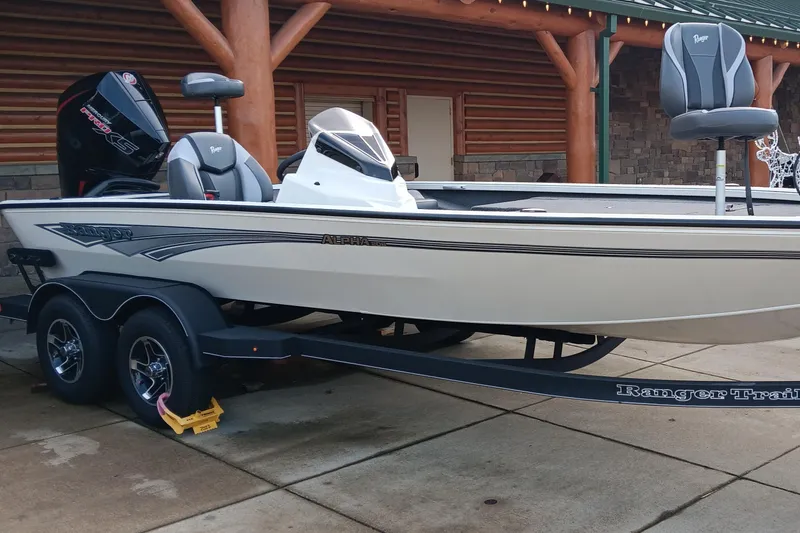 Slide: The Image of 2025 Ranger ALPHA 208 boat on trailer, parked outside log cabin. - 1
