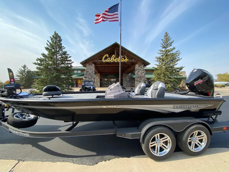 The Image of 2025 Ranger ALPHA 208 boat on trailer outside Cabela's, American flag waving. - 0