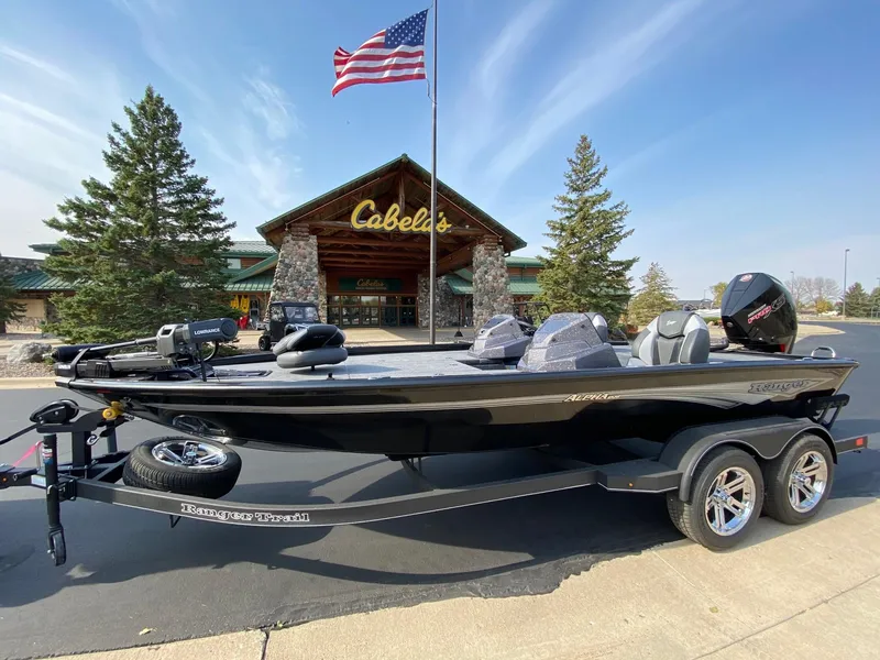 Slide: The Image of 2025 Ranger ALPHA 208 boat on trailer outside Cabela's store with American flag. - 2