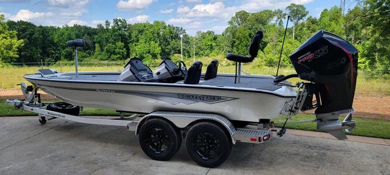 Slide: The Image of 2025 Ranger ALPHA 208 boat on trailer, parked outdoors with lush greenery background. - 2