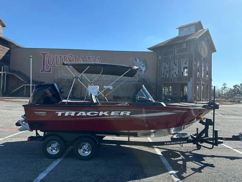 Slide: The Image of 2025 Tracker Targa V-18 WT boat on trailer, parked near rustic building. - 2