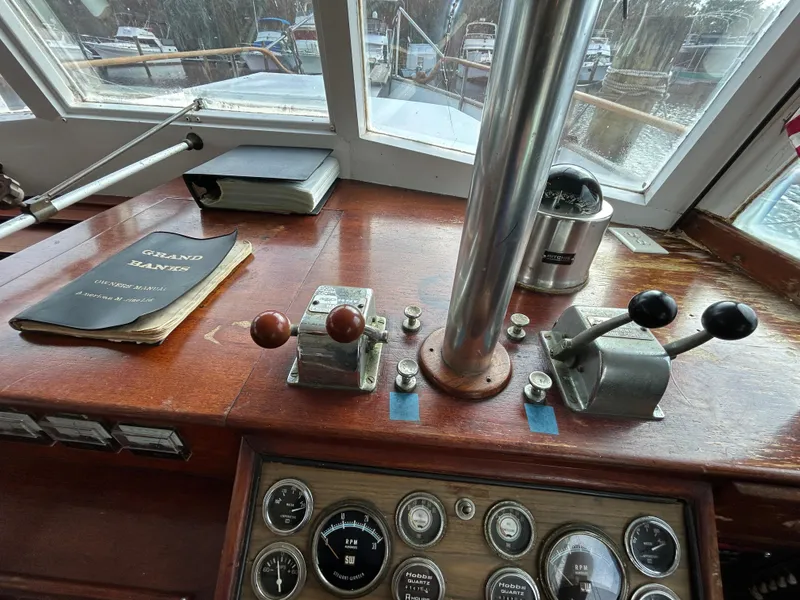 Slide: The Image of 1972 Grand Banks 42 Classic helm with controls, gauges, and manual on wooden dashboard. - 43