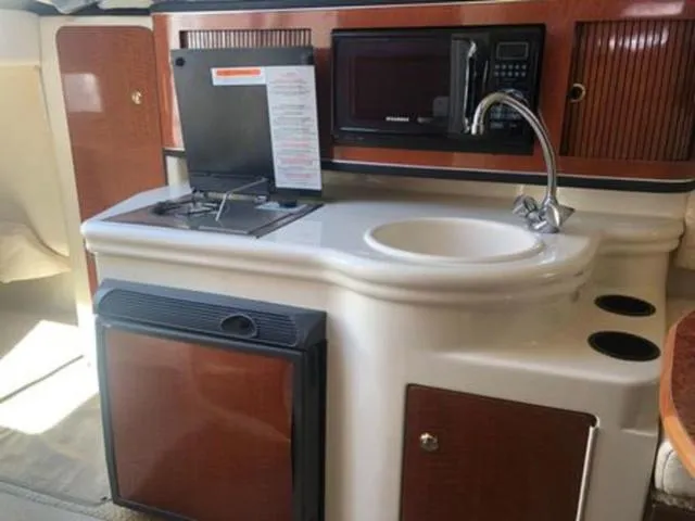 Slide: The Image of 2003 Sea Ray 260 Sundancer kitchenette with sink, stove, microwave, and fridge. - 16