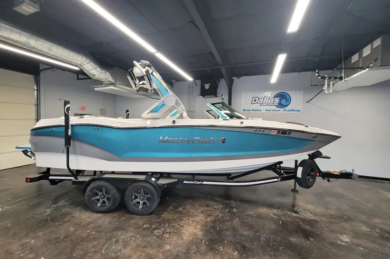 The Image of 2024 MasterCraft X24 boat in showroom, blue and white design, on trailer. - 0