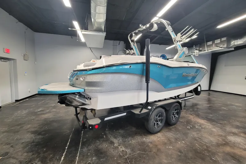 Slide: The Image of 2024 MasterCraft X24 boat in showroom, blue and silver design, on trailer. - 1