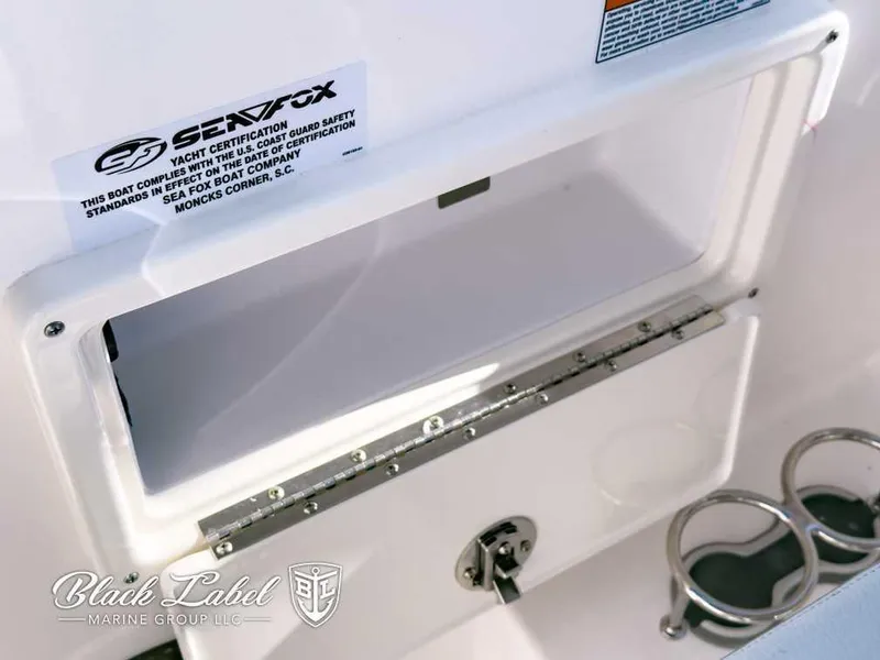 Slide: The Image of Sea Fox 268 Traveler Dual Console 2025 boat storage compartment with cup holders and certification label. - 18