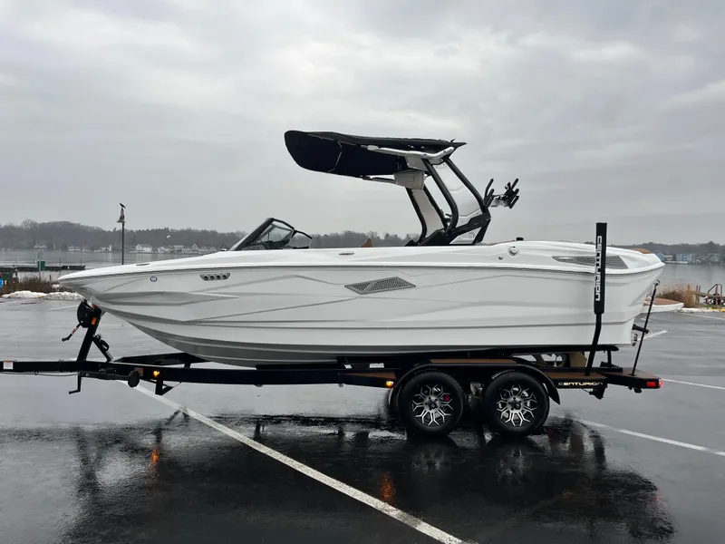 The Image of 2025 Centurion NV213 boat on trailer in rainy parking lot. - 0