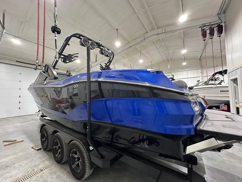 Slide: The Image of 2024 MasterCraft X26 boat in a garage, blue and black design, on a trailer. - 1