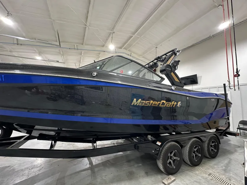 Slide: The Image of 2024 MasterCraft X26 boat in showroom, black with blue accents, on a trailer. - 7