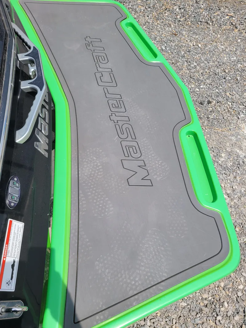 Slide: The Image of 2012 MasterCraft X25 boat platform with green trim on gravel surface. - 13