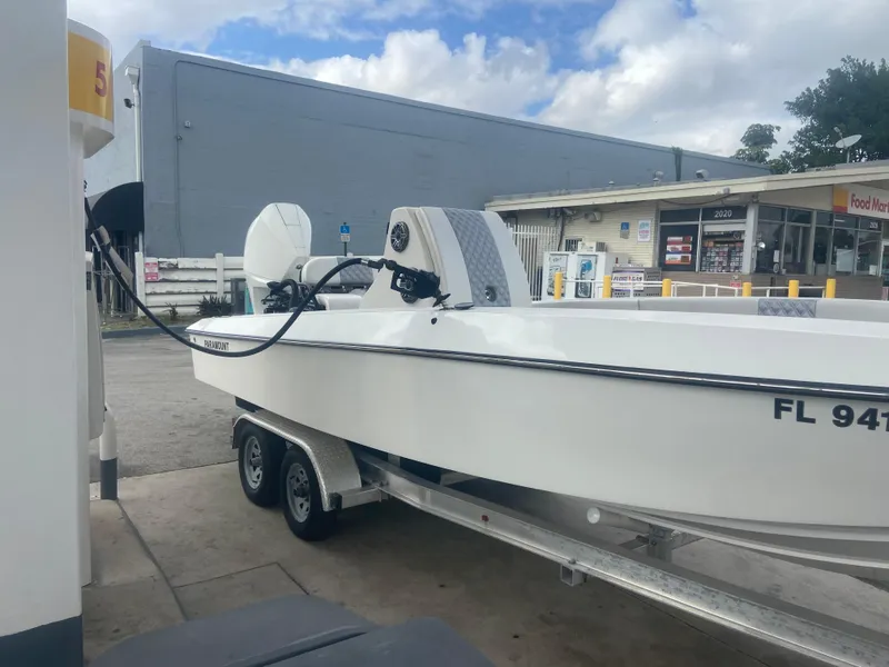 Slide: The Image of 1987 Paramount 21 boat on trailer at gas station, white exterior, overcast sky. - 2