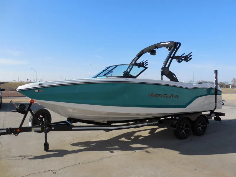 Slide: The Image of 2025 MasterCraft NXT24 boat on trailer, teal and white design, clear sky background. - 5