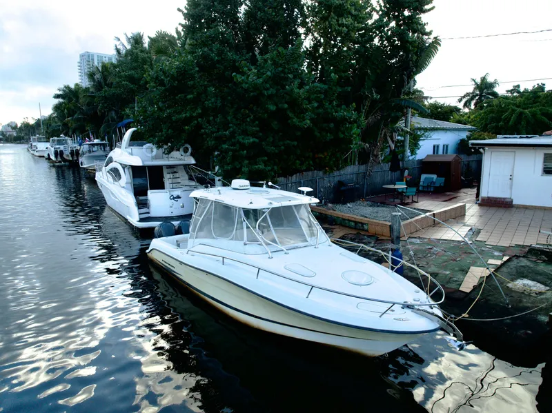 Slide: The Image of 2004 Hydra-Sports Vector 3300 VX boat docked by a canal with lush greenery. - 2