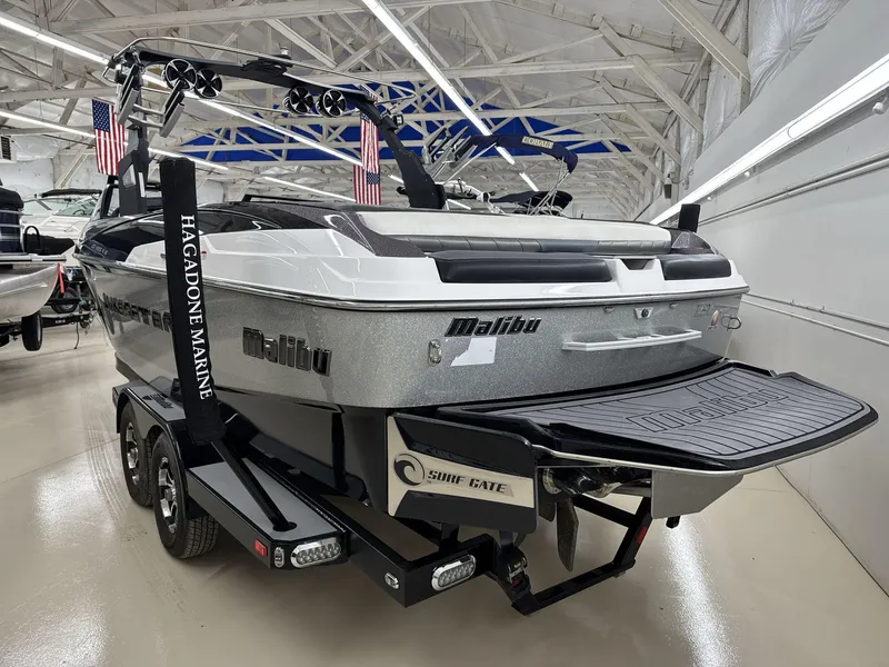 Slide: The Image of 2016 Malibu 25 LSV boat in showroom, featuring Surf Gate and dual-axle trailer. - 5