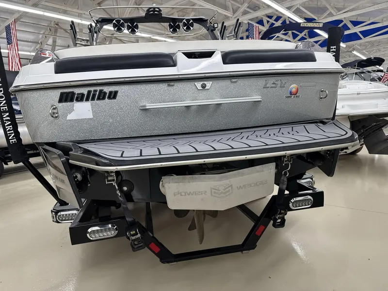 Slide: The Image of 2016 Malibu 25 LSV boat rear view in showroom, featuring Power Wedge and Surf Gate. - 6