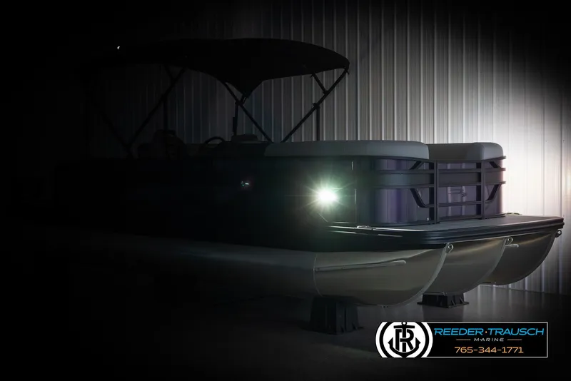 Slide: The Image of 2025 Bennington 23 SSBSE pontoon boat in dimly lit showroom with visible headlight. - 4