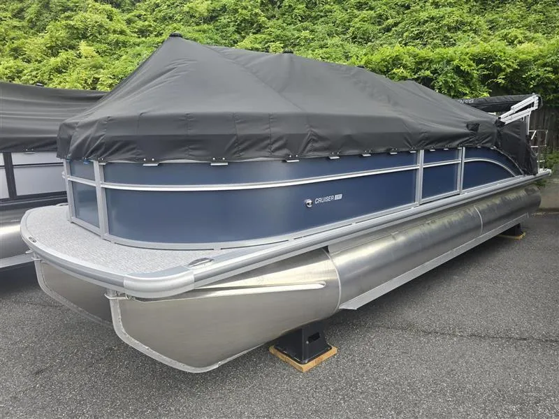 The Image of 2025 Harris Cruiser 230 pontoon boat with black cover, parked on pavement. - 0