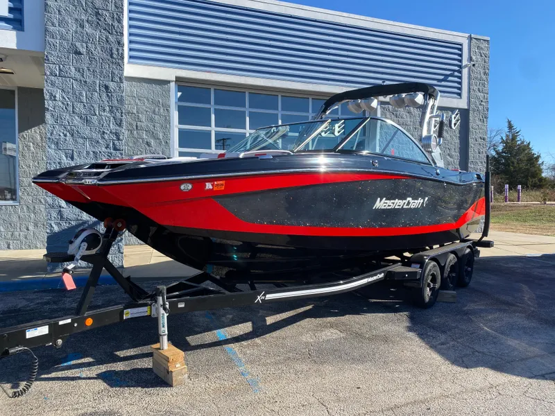 Slide: The Image of 2021 MasterCraft X26 boat on trailer, black and red design, parked outdoors. - 1