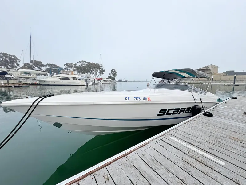 The Image of 1998 Wellcraft Scarab 30 boat docked in a marina, featuring sleek design and canopy. - 0