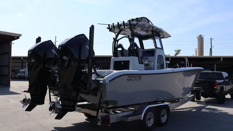 Slide: The Image of 2024 Costa Custom Boats 264 on trailer, featuring dual outboard engines, parked outdoors. - 3