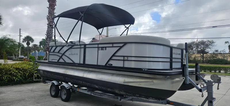 The Image of 2023 Sylvan Mirage X3 Tritoon boat on trailer, parked outdoors under cloudy sky. - 0