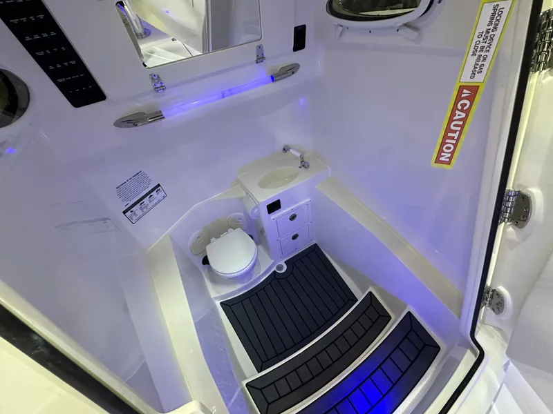 Slide: The Image of 2025 Cobia 301 Center Console boat interior with toilet and sink, featuring blue lighting. - 15