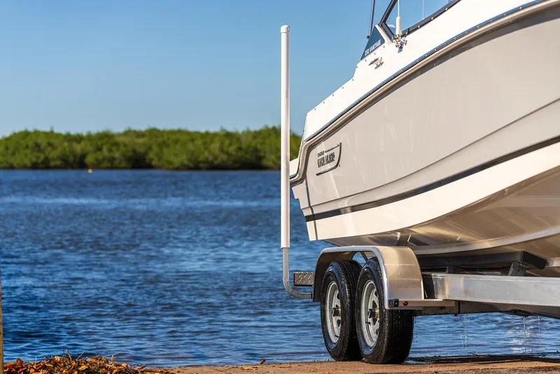 Slide: The Image of 2024 Boston Whaler 210 Vantage boat on trailer by a serene lake. - 26