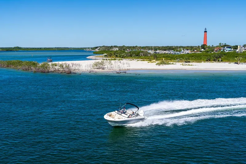 Slide: The Image of 2025 Boston Whaler 210 Vantage cruising near a scenic lighthouse and sandy beach. - 17