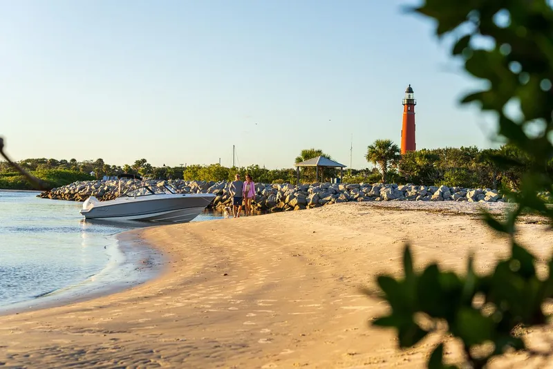 Slide: The Image of Boston Whaler 210 Vantage 2025 near sandy beach with lighthouse in background. - 36