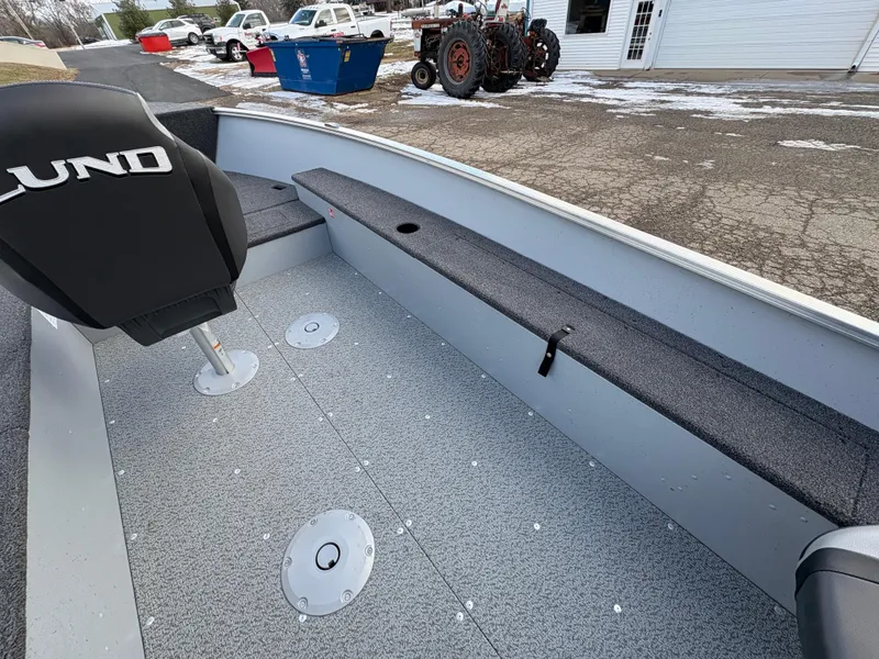Slide: The Image of 2025 Lund 1600 Fury Tiller boat interior with seating and storage, parked outdoors. - 18