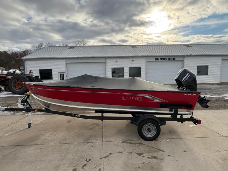 Slide: The Image of 2025 Lund 1600 Fury Tiller boat with cover, parked outside a showroom. - 8