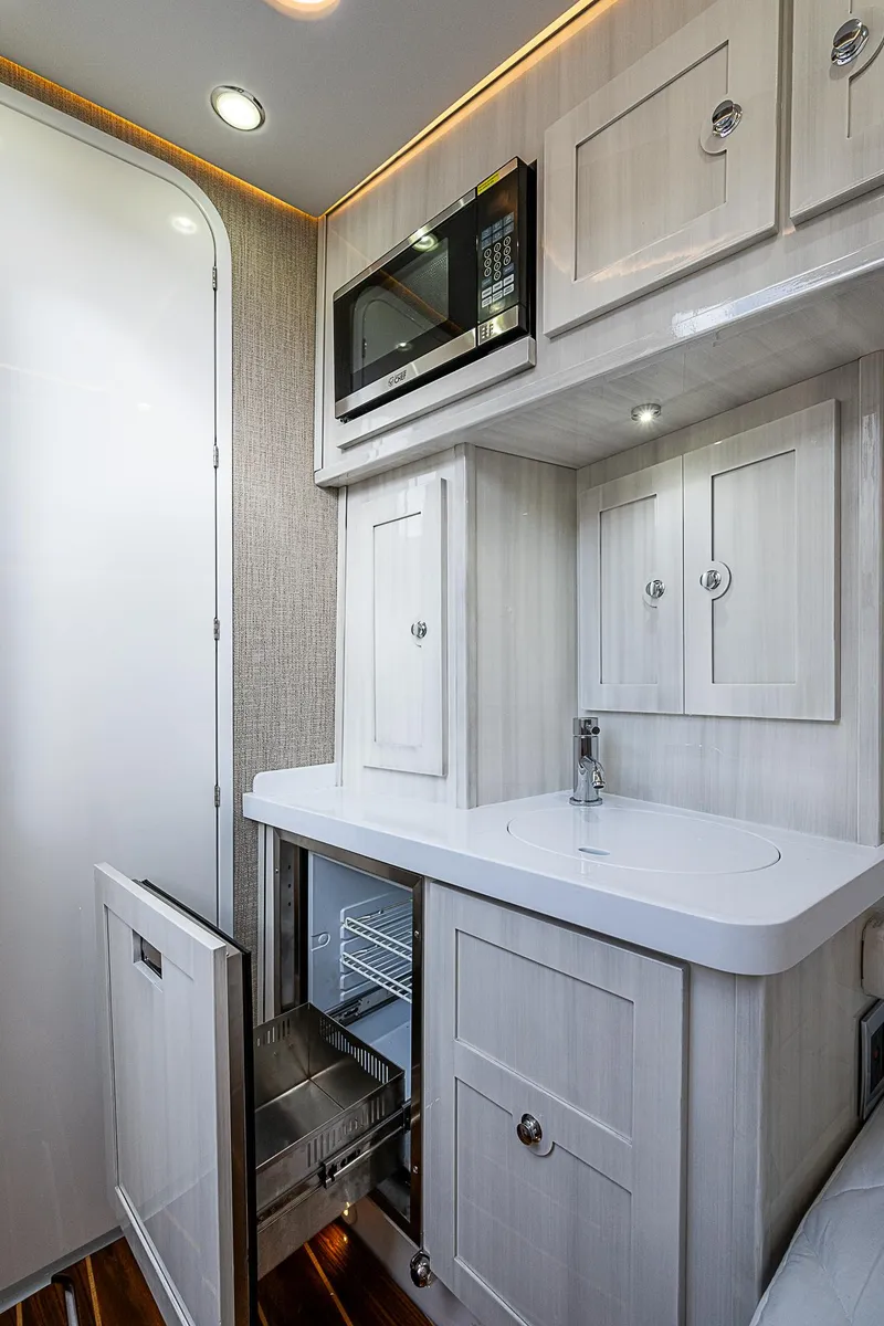 Slide: The Image of 2023 HCB 53 Sueños interior with modern kitchenette, featuring white cabinetry and built-in appliances. - 9