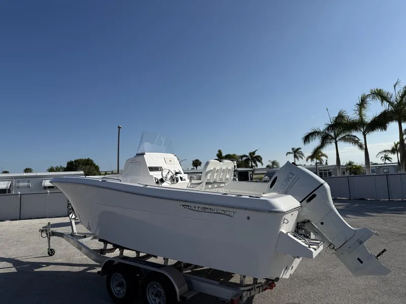 Slide: The Image of 2024 Aquasport 2100 CC boat on trailer, parked outdoors under clear blue sky. - 2