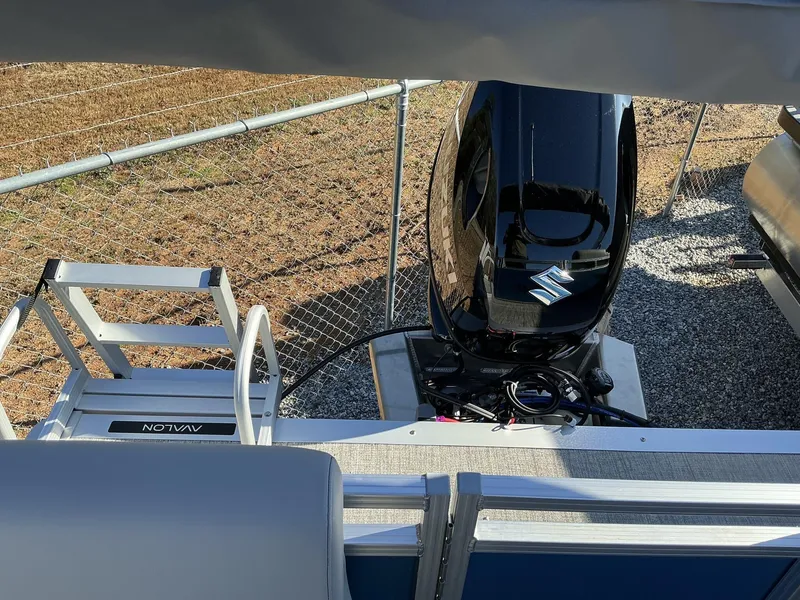 Slide: The Image of 2025 Avalon VLS 23 Quad Lounger with Suzuki outboard motor, parked near a fence. - 6