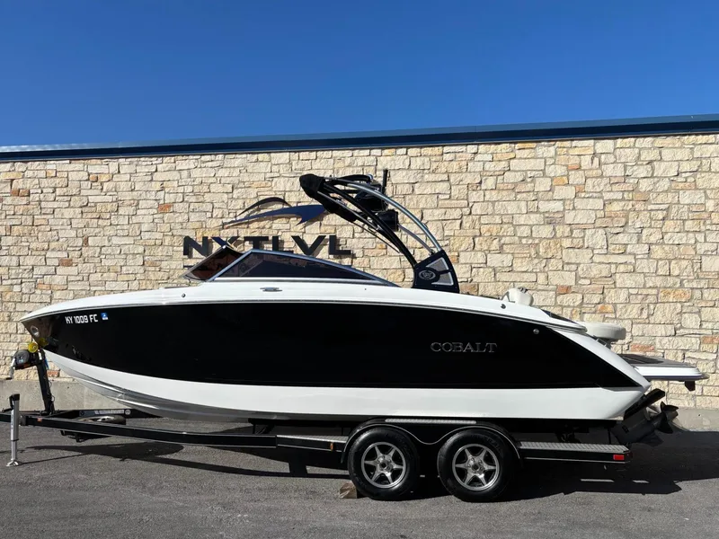 Slide: The Image of 2017 Cobalt R5 boat on trailer, parked against a stone wall under clear blue sky. - 2